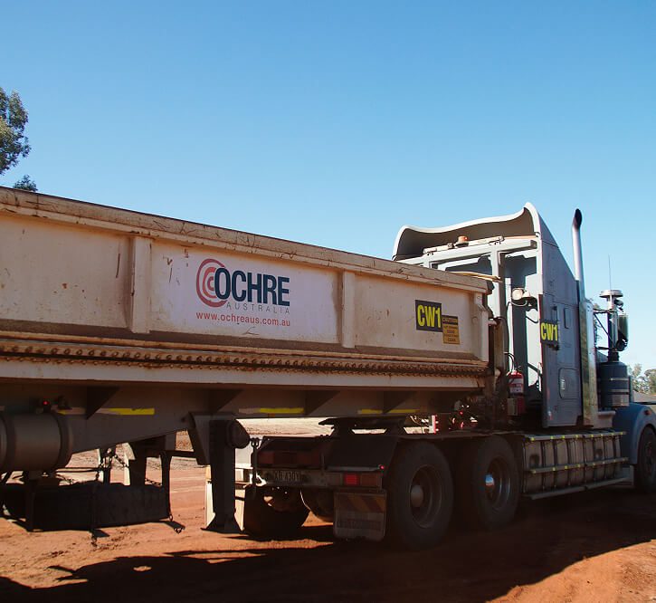 Side view of an Ochre Australia-branded side-tip trailer on a haul truck at a dirt worksite.