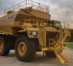 CAT water cart with yellow access stairs parked on site at dusk.